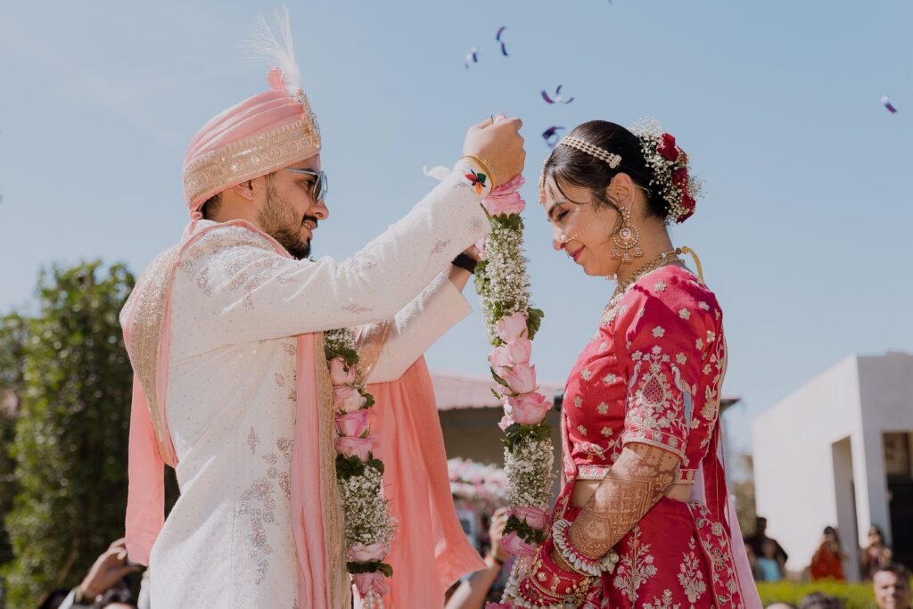 A traditional Indian wedding ceremony outdoors with a bride and groom exchanging flower garlands.